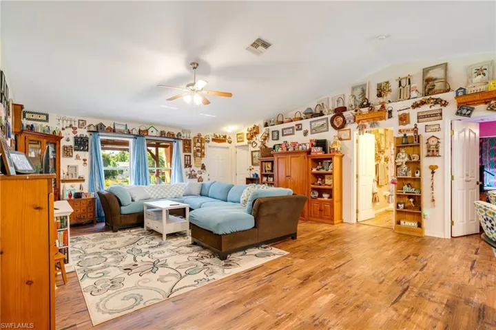 Living room featuring visible vents, light wood-type flooring, a ceiling fan, and vaulted ceiling