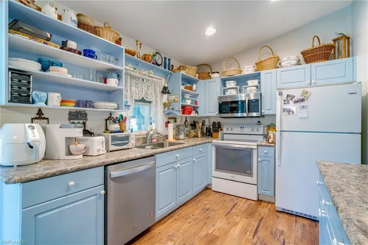 Kitchen with open shelves, light wood-style floors, stainless steel appliances, blue cabinets, and a sink