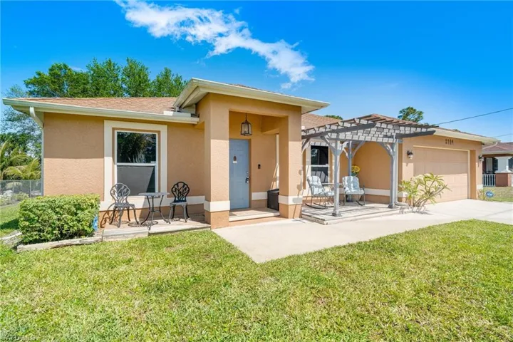 Rear view of house featuring an attached garage, a pergola, stucco siding, a patio area, and a lawn