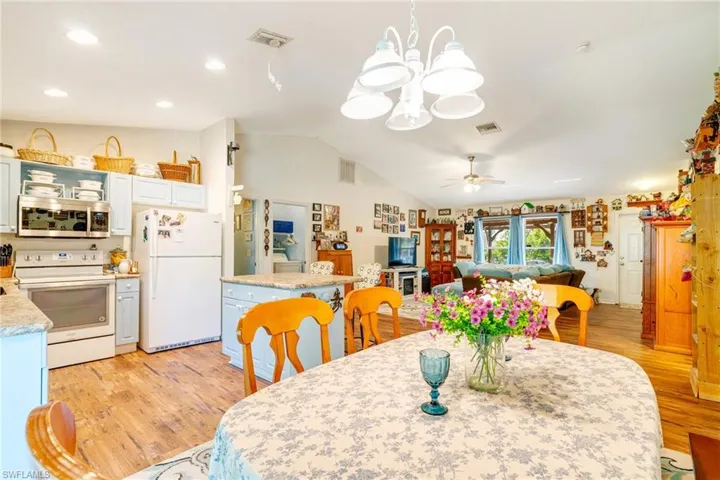 Dining area featuring visible vents, light wood-style flooring, ceiling fan with notable chandelier, and lofted ceiling