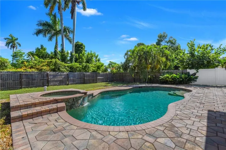 Freeform swimming pool with an integrated spa, surrounded by multi-tone paver decking