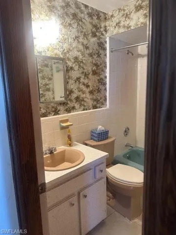 Full bathroom featuring tile patterned floors, toilet, tiled shower / bath, tile walls, and vanity