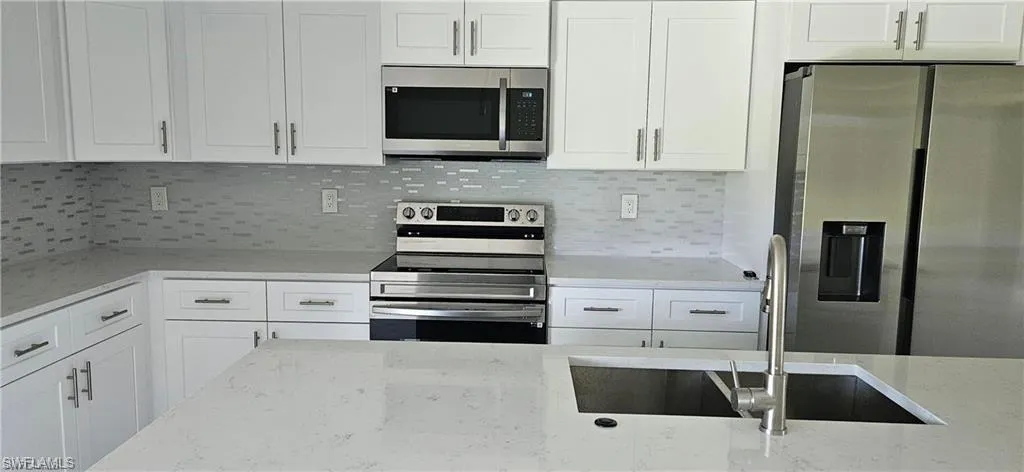 Kitchen with decorative backsplash, stainless steel appliances, and light stone counters