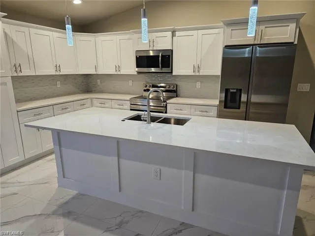 Kitchen featuring decorative light fixtures, sink, white cabinetry, and stainless steel appliances