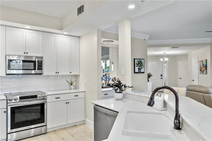Kitchen featuring white cabinetry, hanging light fixtures, light hardwood / wood-style floors, stainless steel appliances, and backsplash