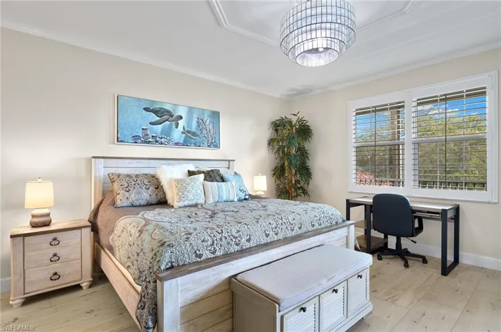 Bedroom with a tray ceiling, light hardwood / wood-style flooring, crown molding, and an inviting chandelier