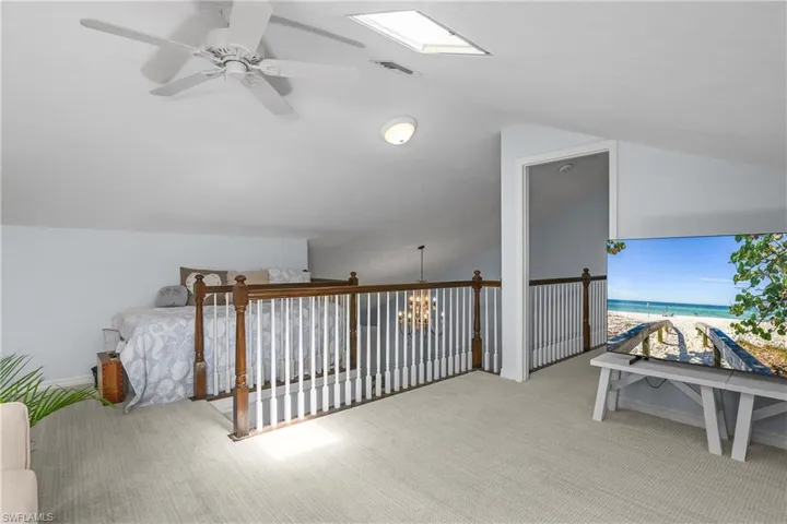 Bonus room with lofted ceiling, light carpet, view of water and beach, a chandelier, and ceiling fan
