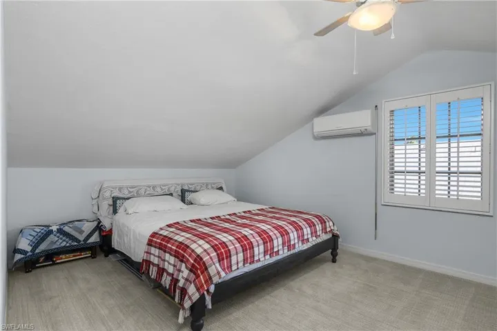 Bedroom with vaulted ceiling, light carpet, a wall unit AC, and a ceiling fan