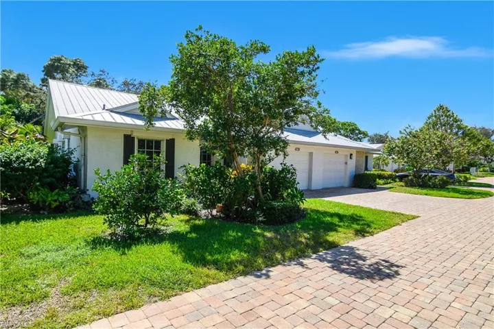View of front of property featuring a front yard, decorative driveway, a standing seam roof, a metal roof, and stucco siding