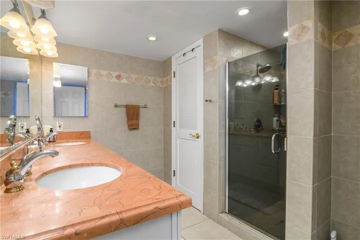 Bathroom featuring tile walls, double vanity, a shower stall, light tile patterned flooring, and recessed lighting