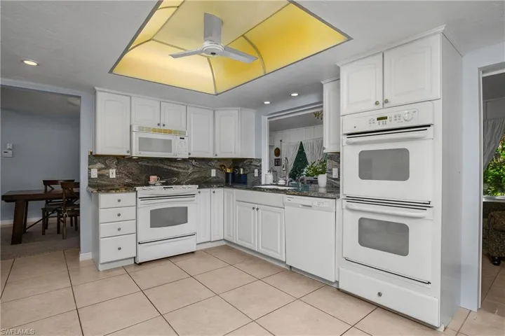 Kitchen featuring white appliances, backsplash, white cabinets, light tile patterned floors, and ceiling fan