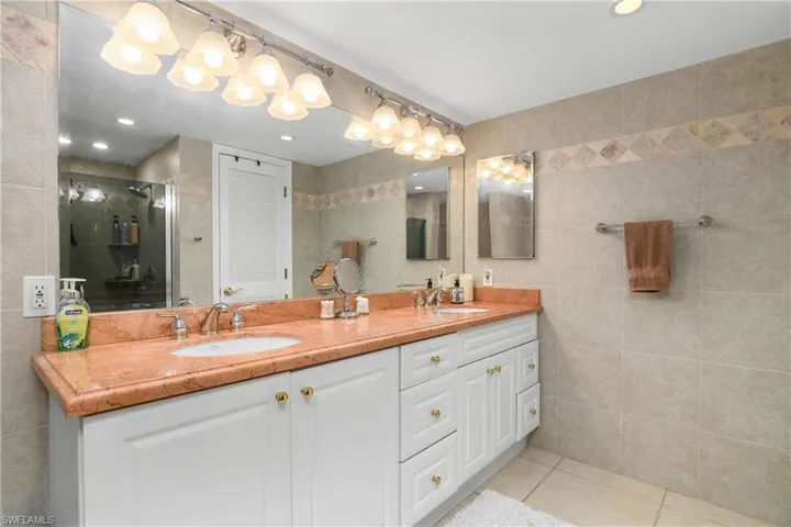 Full bath with tile walls, double vanity, light tile patterned floors, a shower stall, and recessed lighting