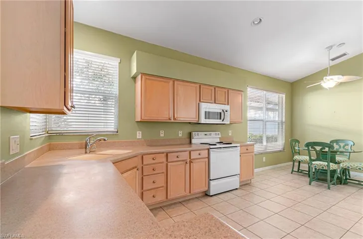 Eat in kitchen with white appliances, light wood finish cabinets, lofted ceiling, light countertops, and ceiling fan