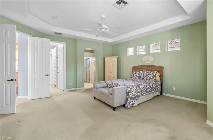 Bedroom with a tray ceiling, light colored carpet, arched walkways, and a ceiling fan