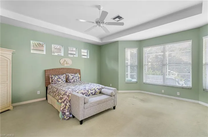 Bedroom featuring a raised ceiling, ceiling fan, a bay area, and multiple windows
