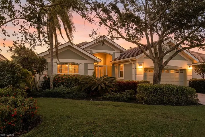 View of front of home with a front lawn, an attached garage, mature landscaping and driveway