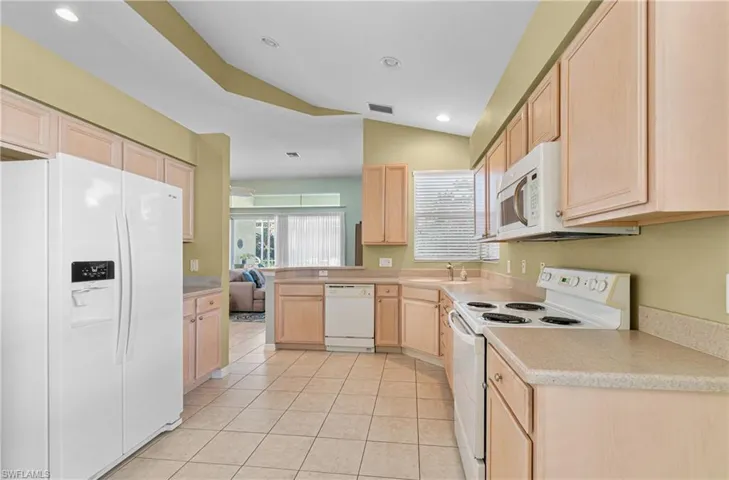 Kitchen with light wood finish cabinetry, white appliances, vaulted ceiling, light countertops, and a peninsula