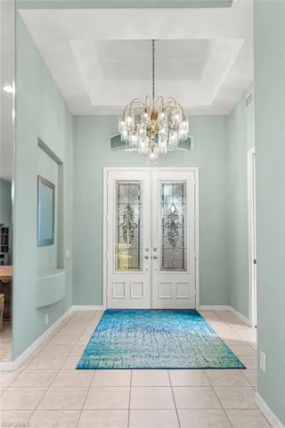 Entryway featuring suspended lighting, a raised ceiling, custom french doors, and light tile patterned flooring