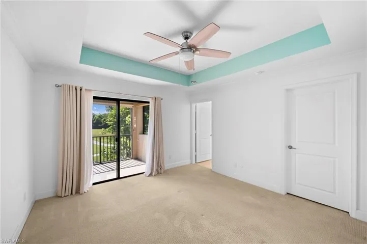 Carpeted empty room featuring ceiling fan, a raised ceiling, and crown molding