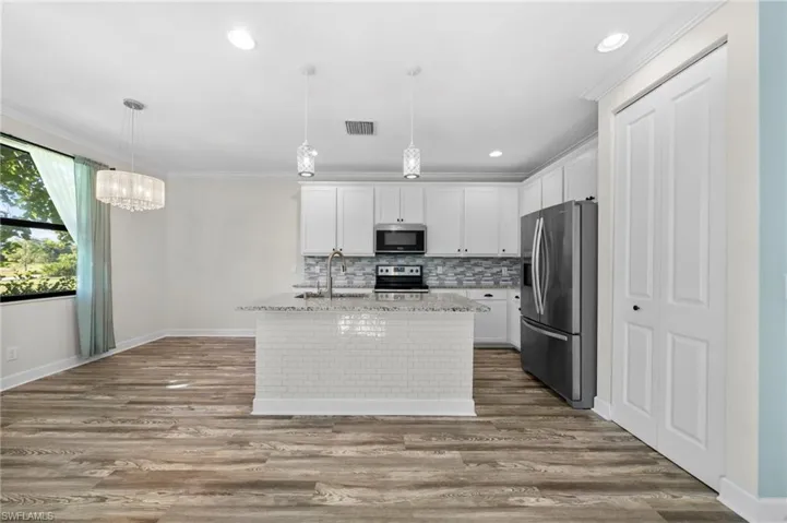 Kitchen with stainless steel appliances, white cabinetry, decorative light fixtures, and a kitchen island with sink