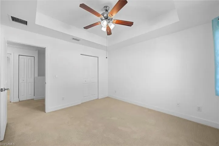 Unfurnished bedroom with light carpet, a closet, a tray ceiling, and ceiling fan