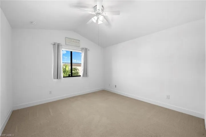 Spare room featuring ceiling fan, vaulted ceiling, and carpet