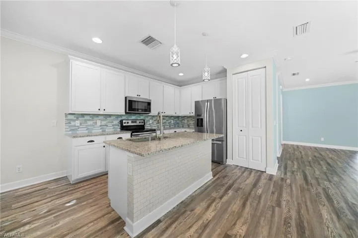 Kitchen featuring an island with sink, appliances with stainless steel finishes, dark hardwood / wood-style floors, and white cabinetry