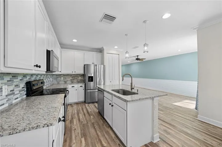 Kitchen featuring ceiling fan, sink, a kitchen island with sink, white cabinetry, and stainless steel appliances