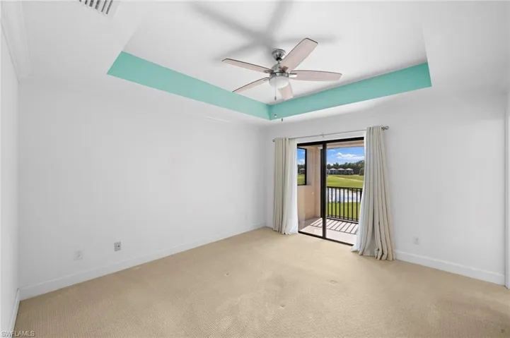 Empty room with light carpet, ceiling fan, and a raised ceiling