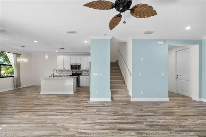 Kitchen with white cabinets, an island with sink, hanging light fixtures, stainless steel appliances, and crown molding