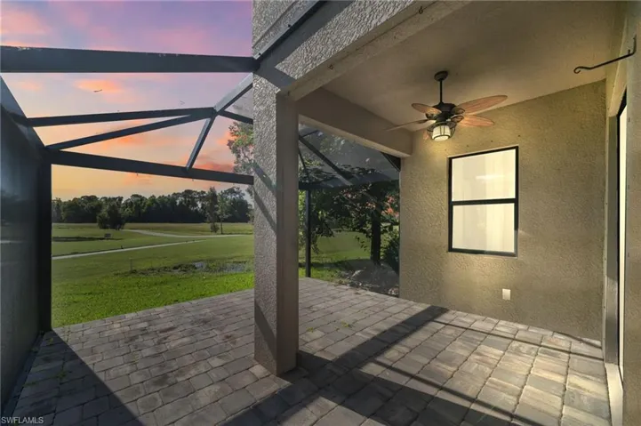 Patio terrace at dusk featuring a lawn, ceiling fan, and a lanai