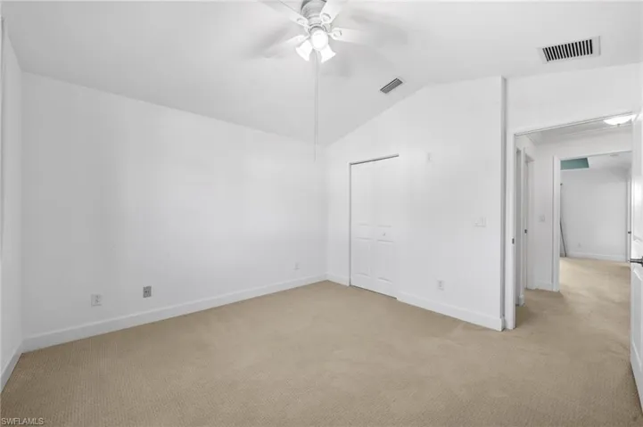 Empty room with lofted ceiling, ceiling fan, and light colored carpet