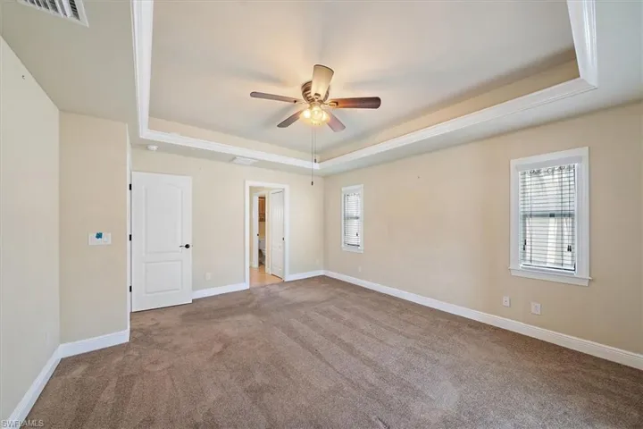 Carpeted master bedroom with ceiling fan and a tray ceiling
