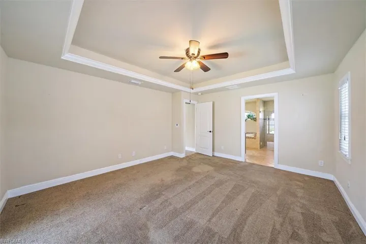 Unfurnished master bedroom with a tray ceiling, master bathroom, carpet flooring, and ceiling fan