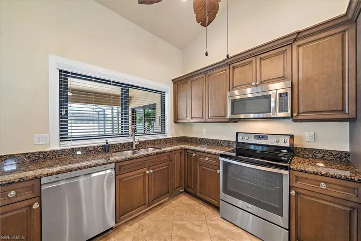 Kitchen featuring dark stone countertops, appliances with stainless steel finishes, sink, ceiling fan, and light tile floors