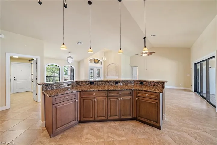 Kitchen with a center island with sink, hanging light fixtures, dark stone counters, and light tile flooring