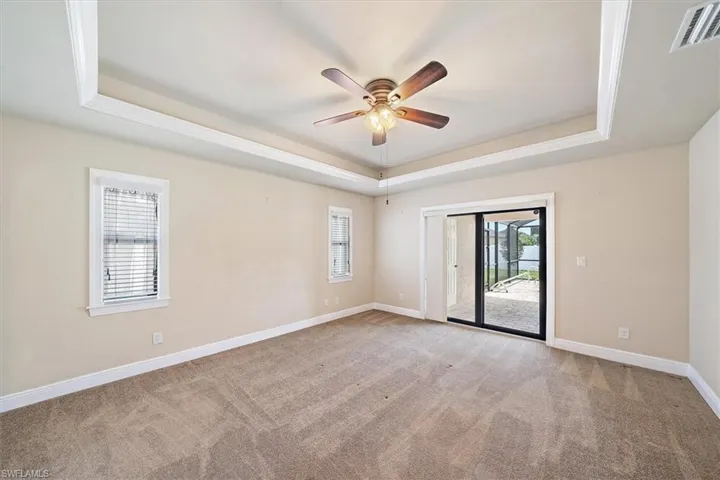 Carpeted master bedroom room featuring plenty of natural light, ceiling fan, and a raised ceiling
