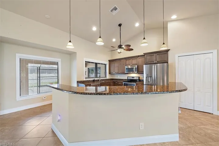 Kitchen with hanging light fixtures, a kitchen island, appliances with stainless steel finishes, high vaulted ceiling, and light tile flooring