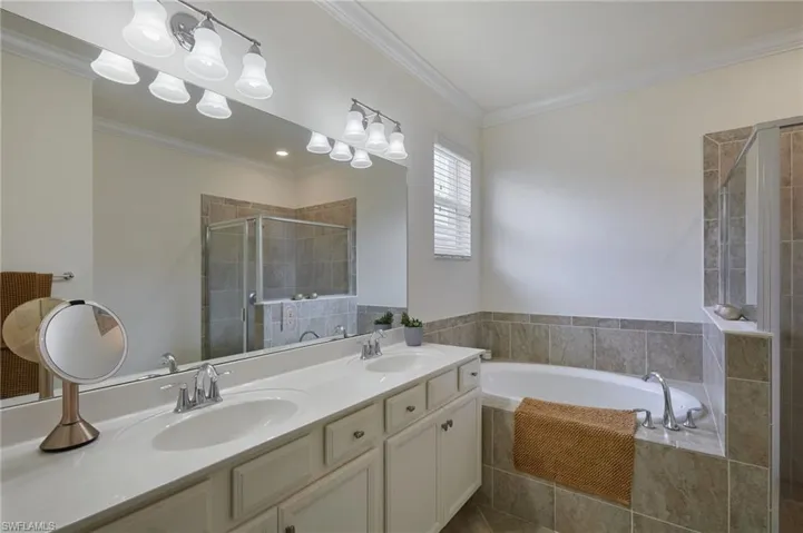 Full bathroom featuring a bath, a double sink, a stall shower, and crown molding