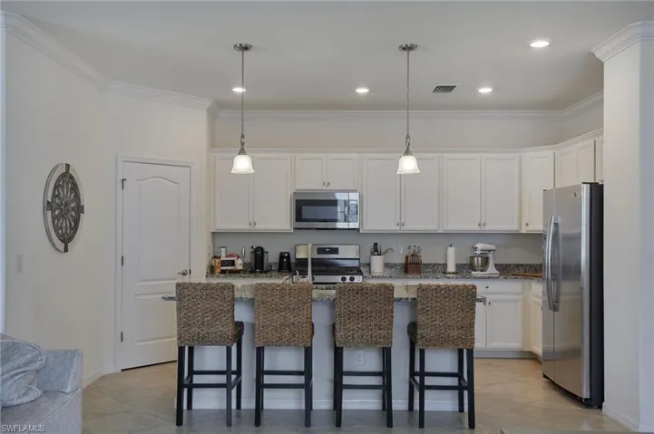 Kitchen featuring white cabinetry, stainless steel appliances, ornamental molding, a breakfast bar