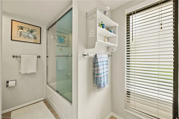 Bathroom with shower / bath combination with glass door, visible vents, and baseboards