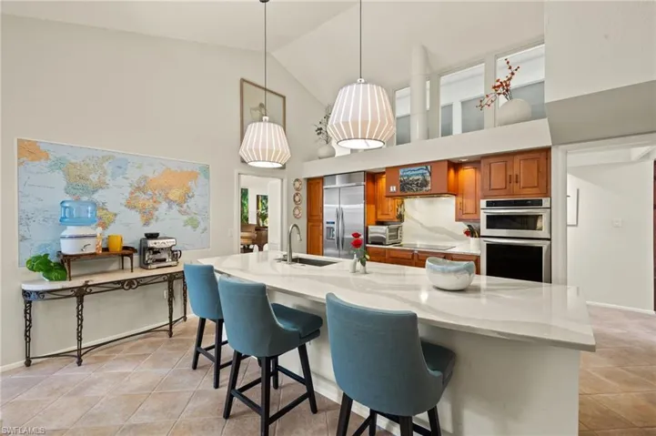 Kitchen with light stone counters, a sink, appliances with stainless steel finishes, brown cabinets, and decorative light fixtures