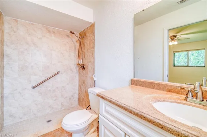 Bathroom featuring tiled shower, vanity, ceiling fan, and toilet