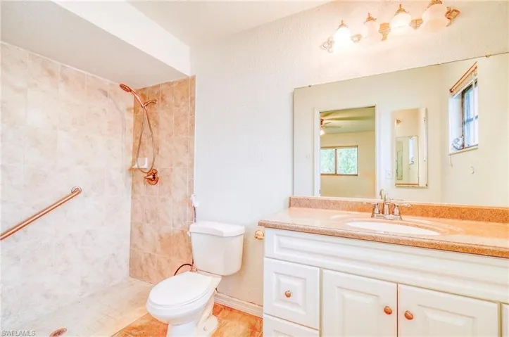 Bathroom featuring a textured ceiling, toilet, vanity, ceiling fan, and a tile shower