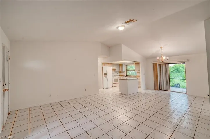 Unfurnished living room with light tile patterned flooring, a notable chandelier, and high vaulted ceiling