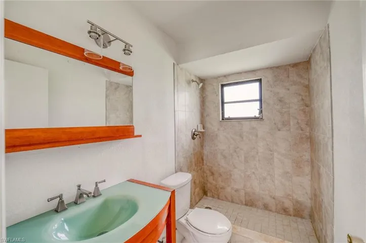 Bathroom featuring tiled shower, toilet, and vanity