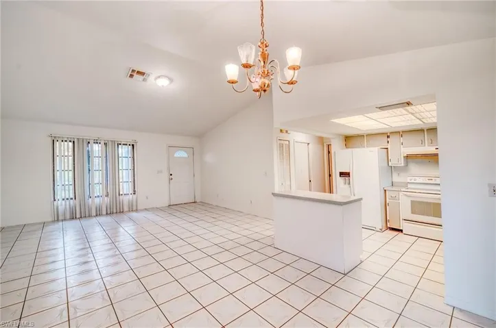 Kitchen with white appliances, pendant lighting, white cabinetry, light tile patterned flooring, and a chandelier