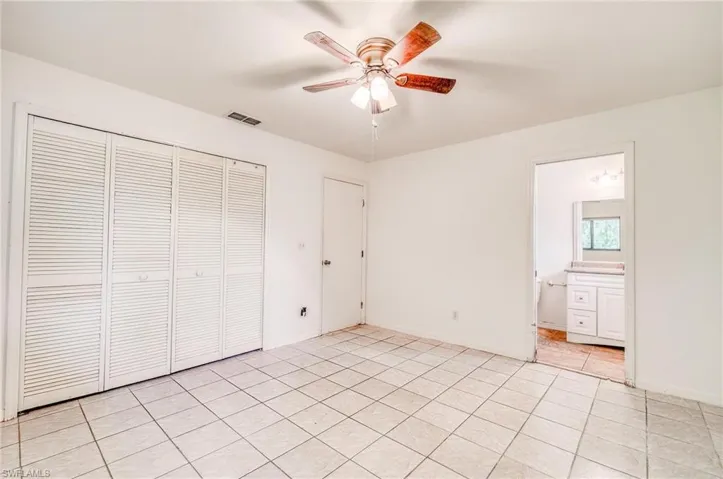 Unfurnished bedroom featuring a closet, light tile patterned flooring, ensuite bathroom, and ceiling fan