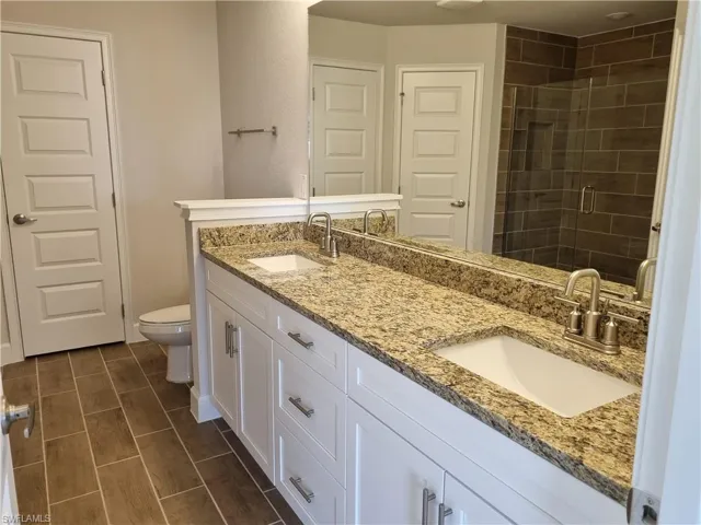 Bathroom featuring toilet, double vanity, and a shower stall