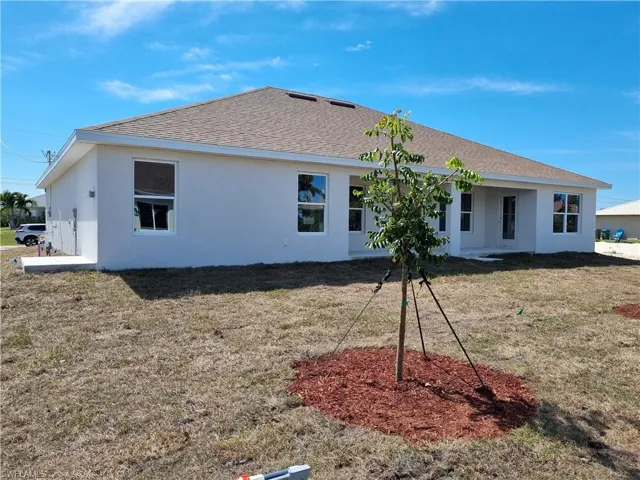 Back of property with stucco siding, a lawn, and roof with shingles
